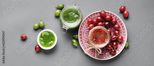 Jars and bowl with tasty gooseberry jam on grey background  top view