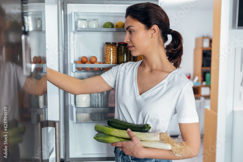 Beautiful young woman taking some healthy food from the fridge in the kitchen at home photo