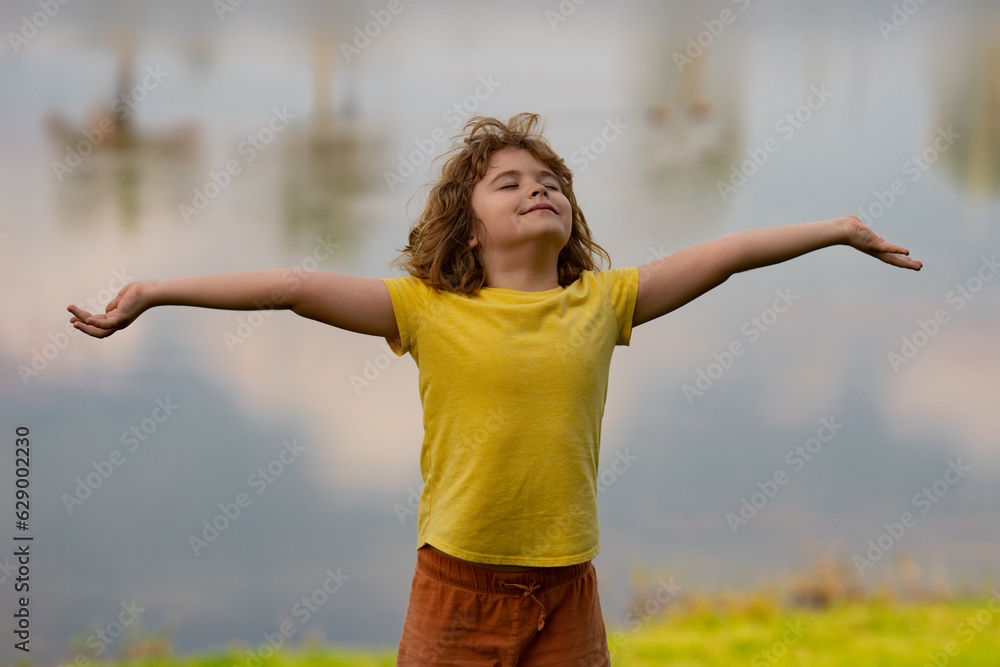 Little kid boy raising hands enjoying life and summer nature. Happy kid looking on summer sun. Fresh air, environment concept. Dream of flying. Summer seasonal outdoor. Carefree child enjoys summer Little kid boy raising hands enjoying life and summer nature. Happy kid looking on summer sun. Fresh air, environment concept. Dream of flying. Summer seasonal outdoor. Carefree child enjoys summer