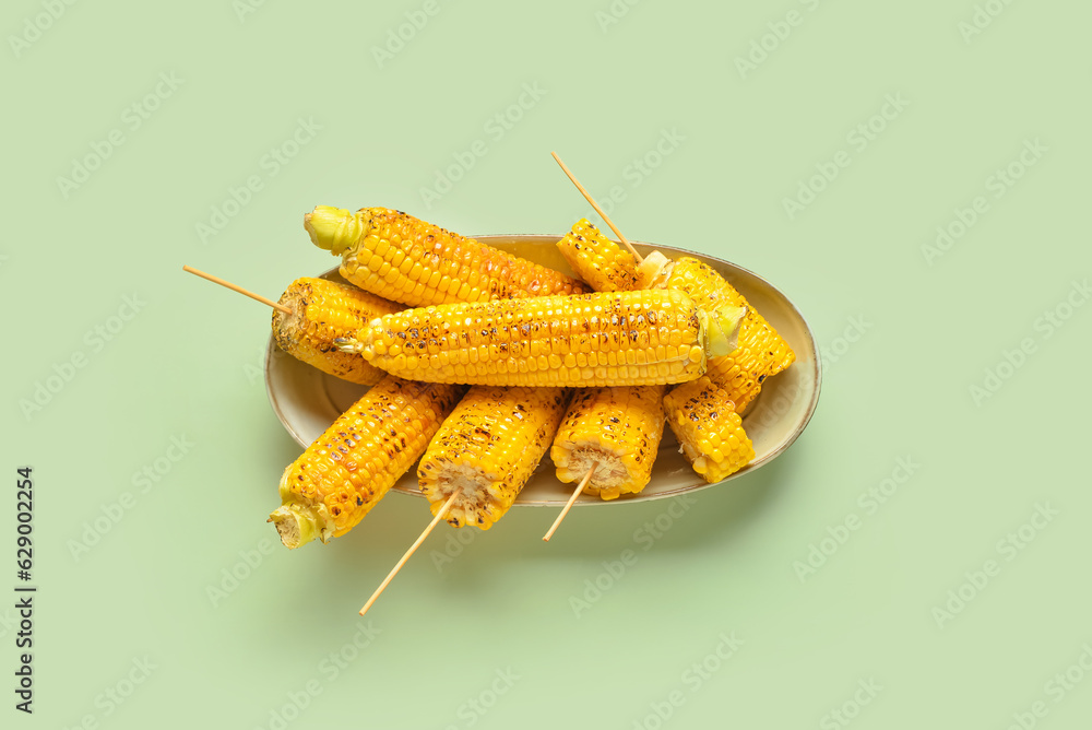 Bowl with tasty grilled corn cobs on green background