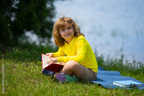 Smart clever Kids. Cute child read books outdoors. Kids learning and summer education. Child boy reading book outdoor on green grass field. Child is learning and reading. Kid read book in the garden.