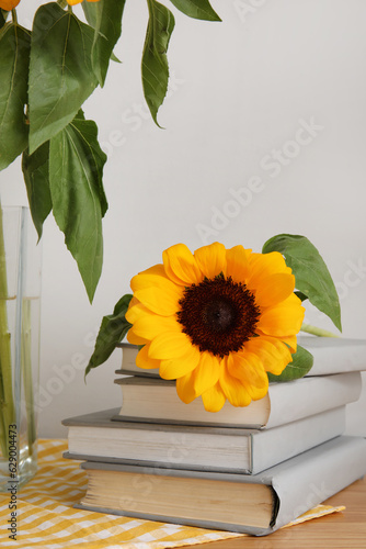 Beautiful sunflower with books on shelf near light wall