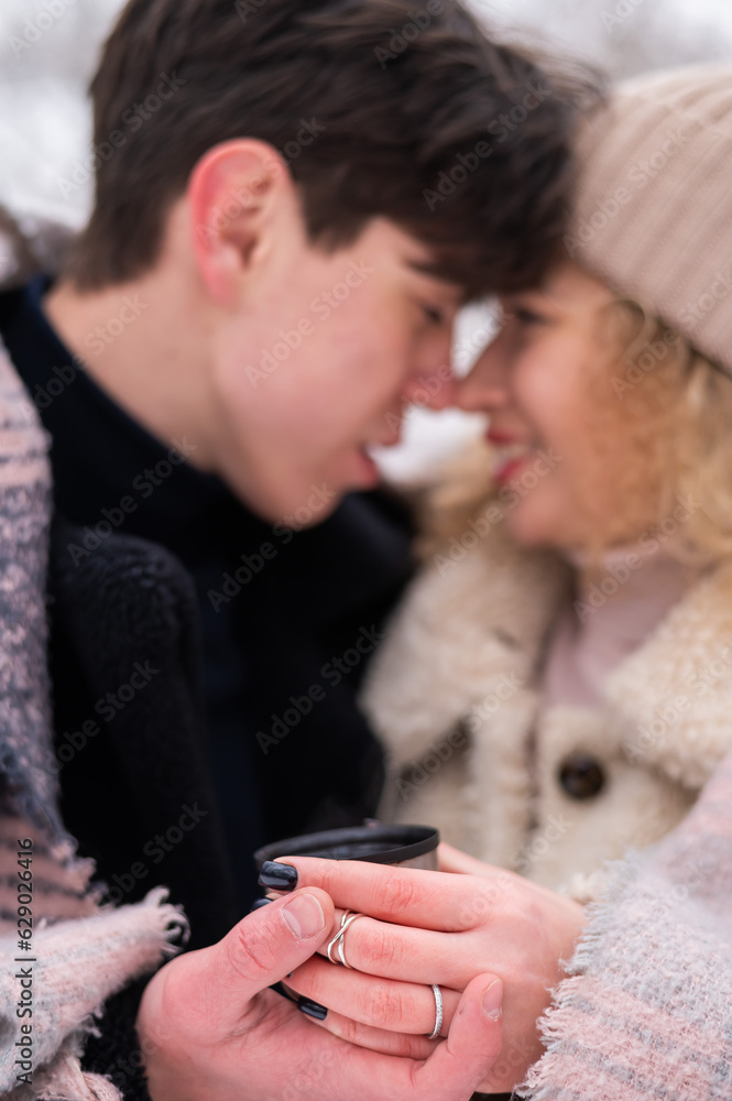 A young couple walks in the park in winter. The guy and the girl are drinking a warming drink outdoors. A young couple walks in the park in winter. The guy and the girl are drinking a warming drink outdoors.