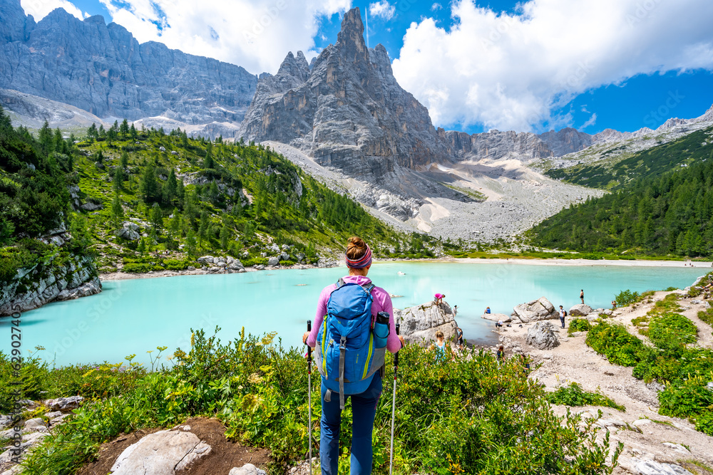 Young sportive woman enjoys beautiful view on the turquoise Sorapis lake in the morning. Lake Sorapis, Dolomites, Belluno, Italy, Europe. Young sportive woman enjoys beautiful view on the turquoise Sorapis lake in the morning. Lake Sorapis, Dolomites, Belluno, Italy, Europe.