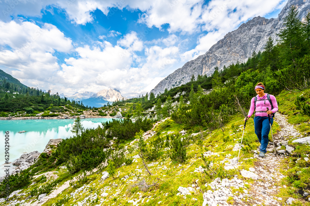 Young sportive woman walkes along hiking trail at the beautiful turquoise Sorapis lake in the afternoon. Lake Sorapis, Dolomites, Belluno, Italy, Europe. Young sportive woman walkes along hiking trail at the beautiful turquoise Sorapis lake in the afternoon. Lake Sorapis, Dolomites, Belluno, Italy, Europe.