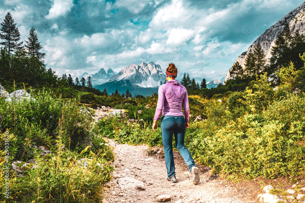 Athletic woman walks on hiking trail at Sorapis lake with impressive view on Cadini di Misurina in the background in the evening. Lake Sorapis, Dolomites, Belluno, Italy, Europe.