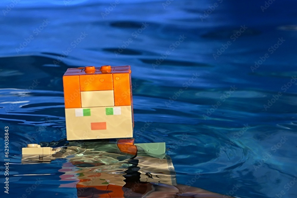 Naklejka premium LEGO Minecraft large action figure of main character Alex relaxing in deep blue water of summer swimming pool.