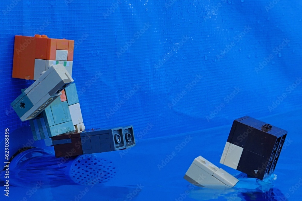 Obraz premium LEGO Minecraft figure of Alex sitting on blue pool filter plastic sifter cover, raising hand to Steve swimming towards her