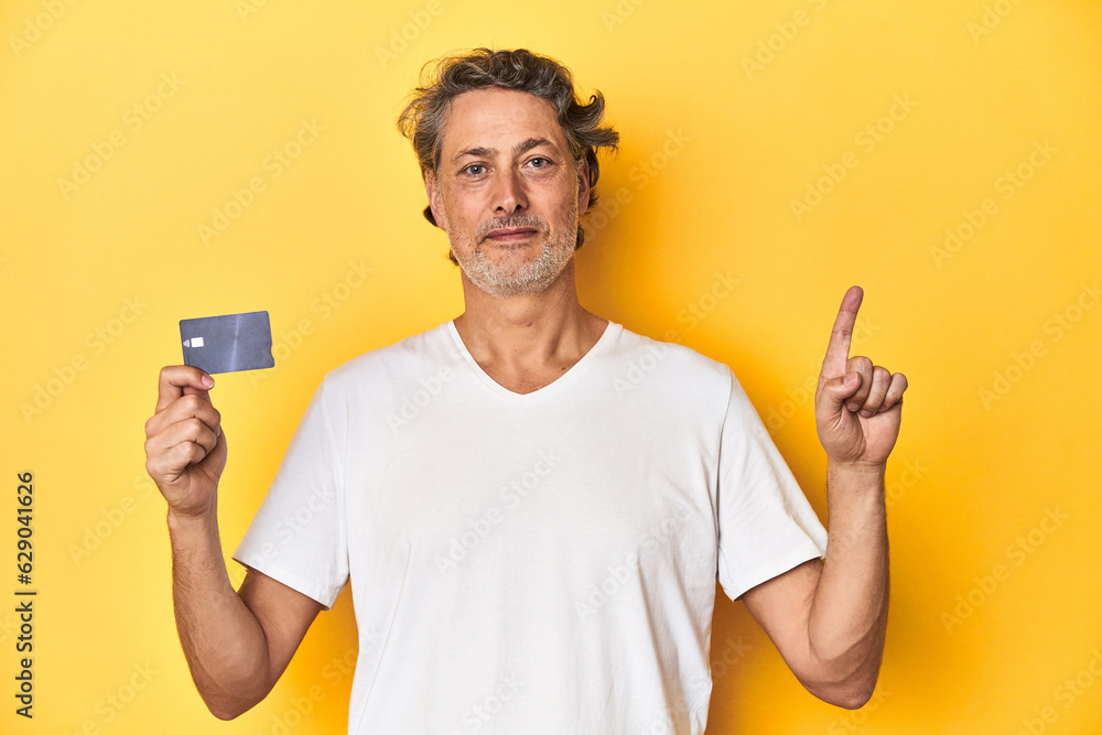 Man holding a credit card, yellow studio backdrop showing number one with finger. Man holding a credit card, yellow studio backdrop showing number one with finger.