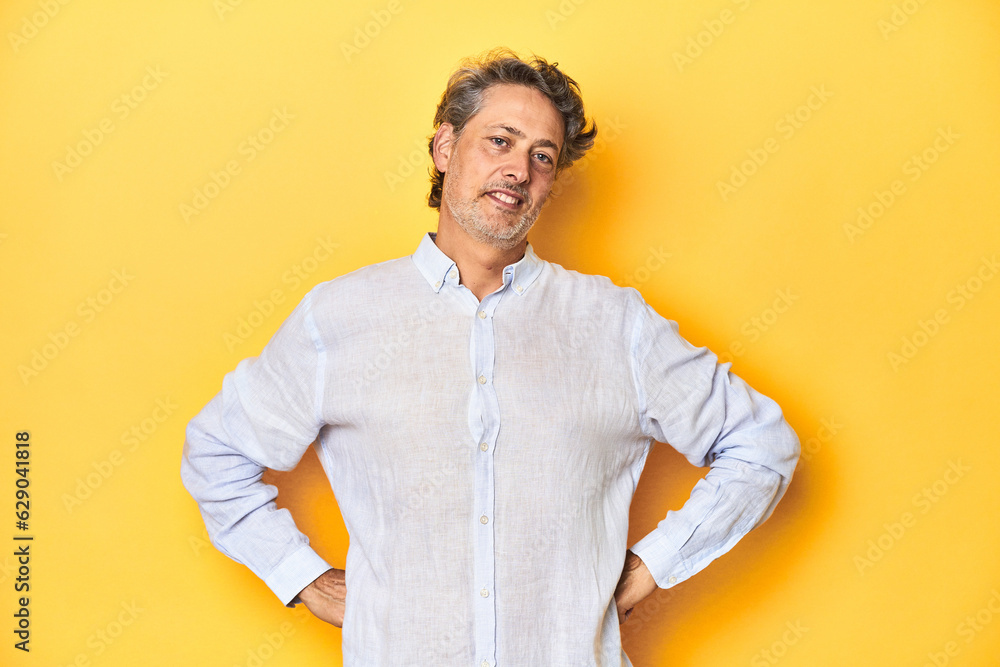 Middle-aged man posing on a yellow backdrop confident keeping hands on hips. Middle-aged man posing on a yellow backdrop confident keeping hands on hips.