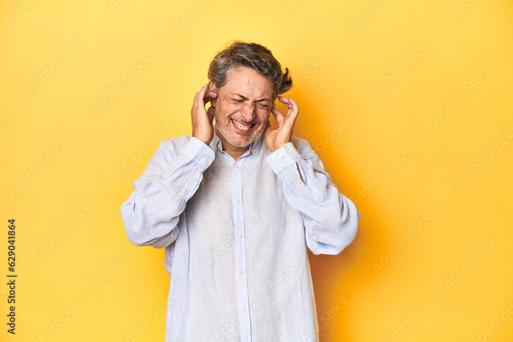 Middle-aged man posing on a yellow backdrop covering ears with hands. Middle-aged man posing on a yellow backdrop covering ears with hands.