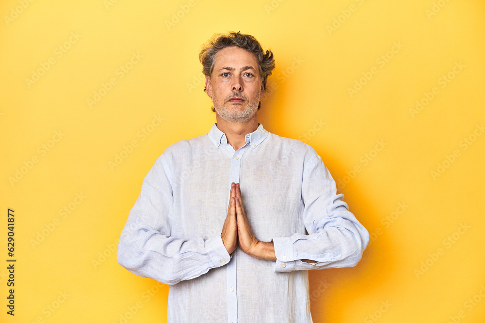 Middle-aged man posing on a yellow backdrop praying, showing devotion, religious person looking for divine inspiration. Middle-aged man posing on a yellow backdrop praying, showing devotion, religious person looking for divine inspiration.