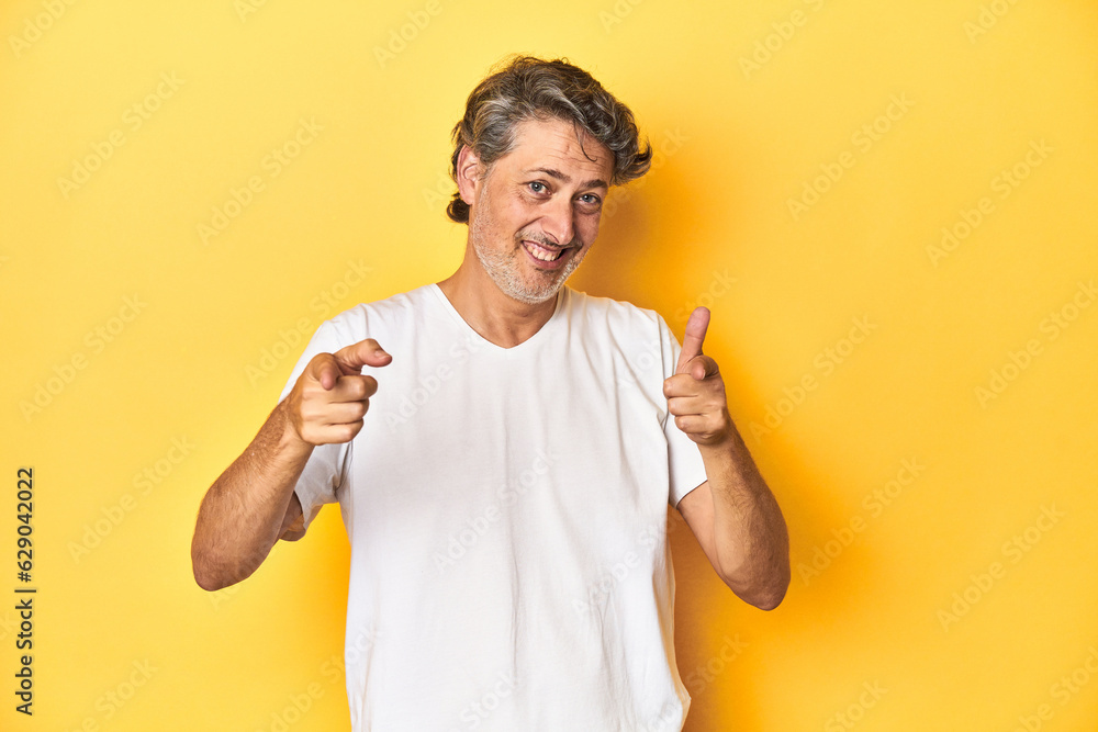 Middle-aged man posing on a yellow backdrop pointing to front with fingers. Middle-aged man posing on a yellow backdrop pointing to front with fingers.