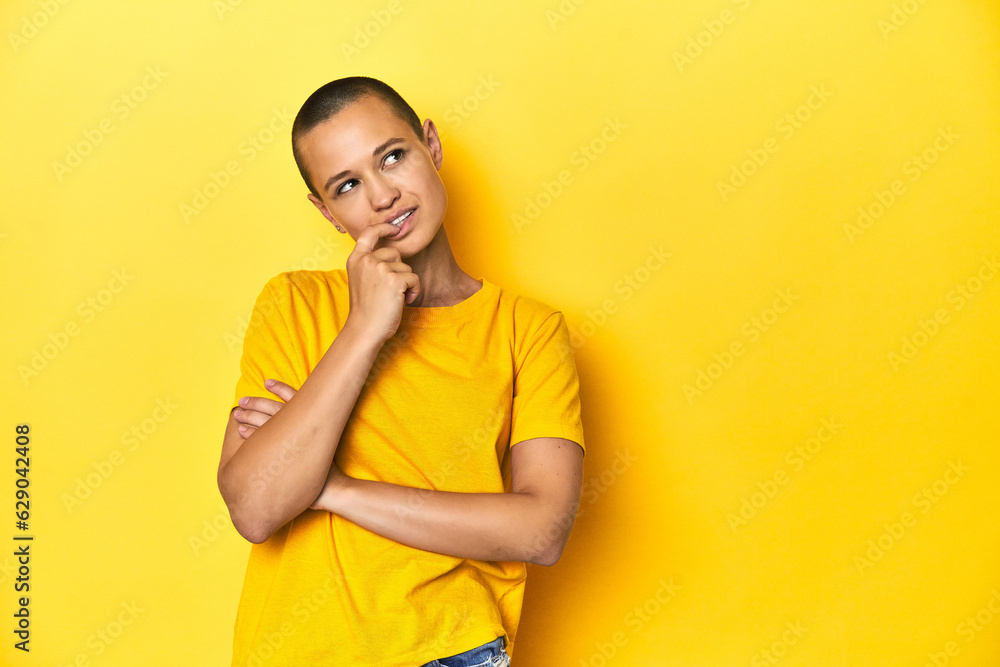 Young woman in yellow tee, yellow studio backdrop relaxed thinking about something looking at a copy space. Young woman in yellow tee, yellow studio backdrop relaxed thinking about something looking at a copy space.