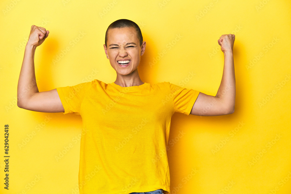 Young woman in yellow tee, yellow studio backdrop raising fist after a victory, winner concept. Young woman in yellow tee, yellow studio backdrop raising fist after a victory, winner concept.