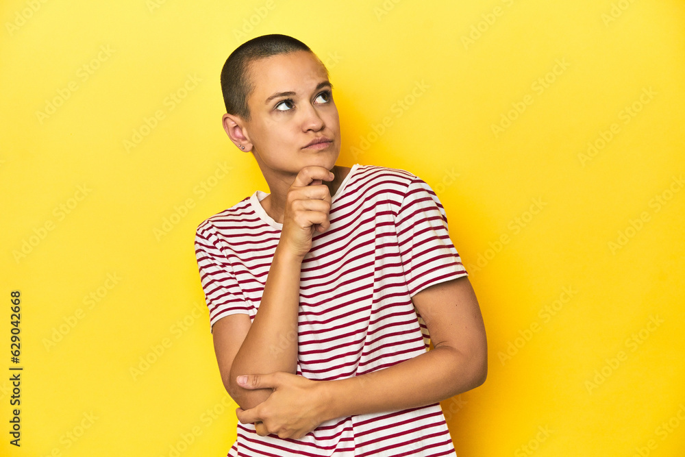 Shaved head woman in red striped tee, yellow backdrop thinking and looking up, being reflective, contemplating, having a fantasy. Shaved head woman in red striped tee, yellow backdrop thinking and looking up, being reflective, contemplating, having a fantasy.
