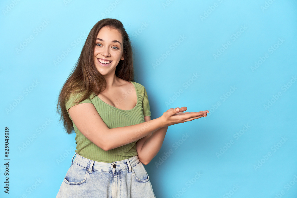 Young Caucasian woman in a green top on a blue backdrop holding a copy space on a palm. Young Caucasian woman in a green top on a blue backdrop holding a copy space on a palm.