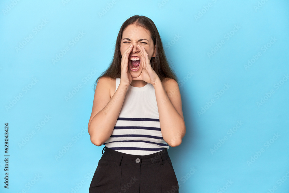 Woman in a striped top posing on a blue studio backdrop shouting excited to front. Woman in a striped top posing on a blue studio backdrop shouting excited to front.