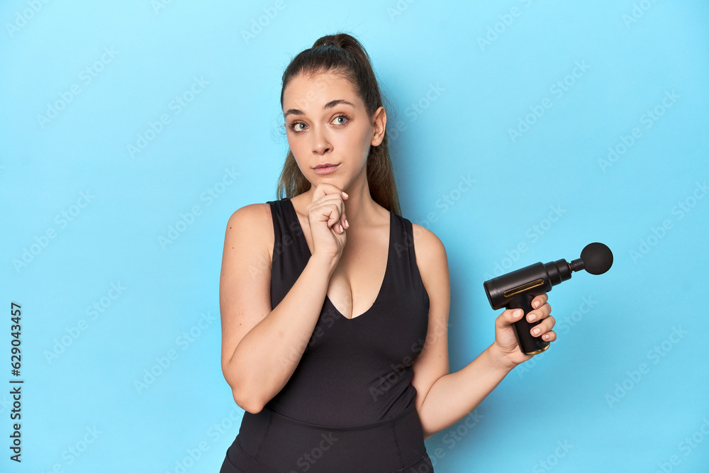 Active woman with an electric massager in a blue studio looking sideways with doubtful and skeptical expression. Active woman with an electric massager in a blue studio looking sideways with doubtful and skeptical expression.
