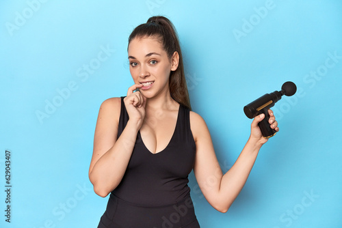 Active woman with an electric massager in a blue studio relaxed thinking about something looking at a copy space.