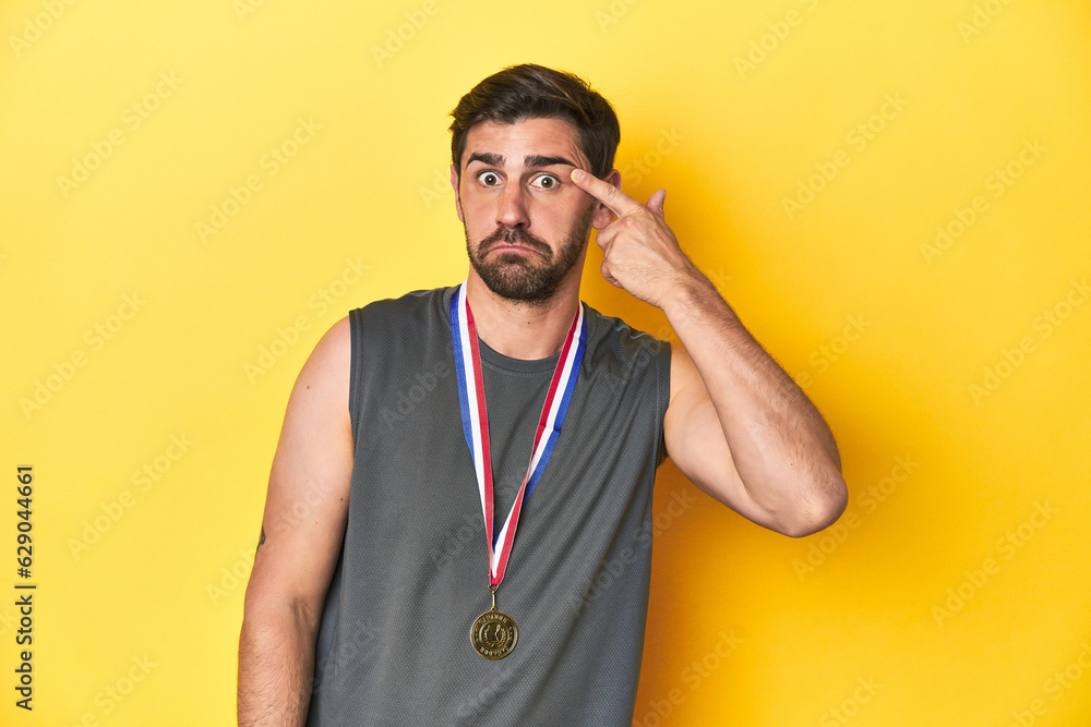 Athletic man with gold medal, yellow studio backdrop showing a disappointment gesture with forefinger. Athletic man with gold medal, yellow studio backdrop showing a disappointment gesture with forefinger.