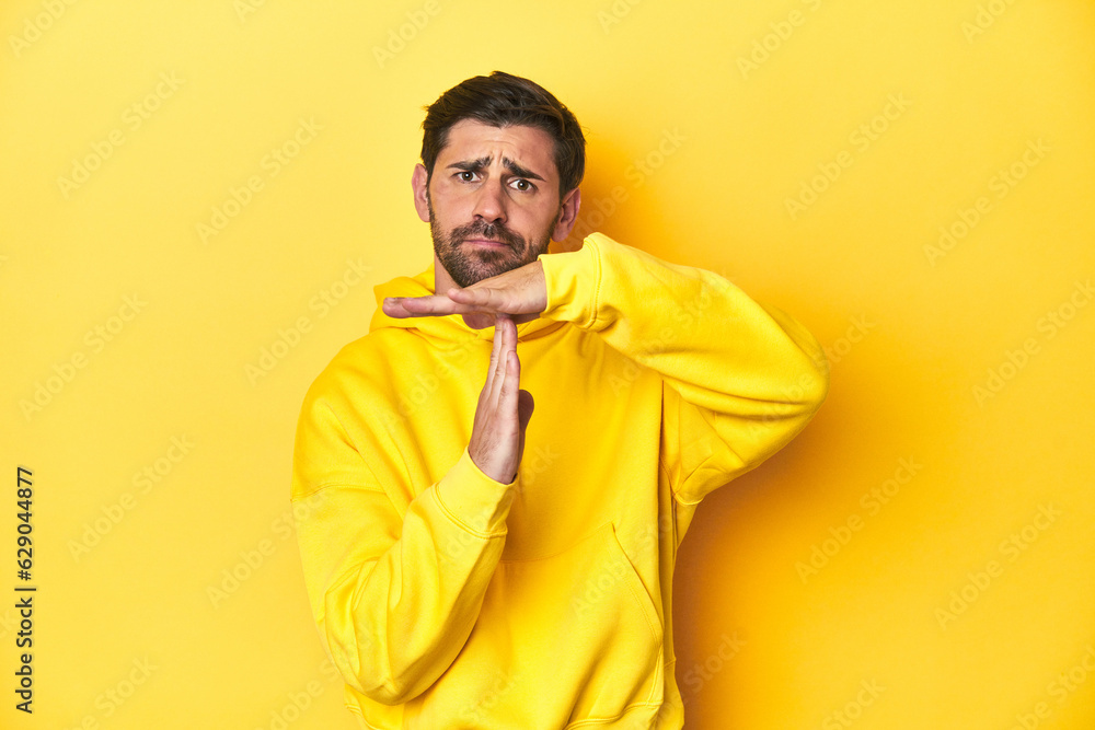 Man in yellow hoodie, monochrome studio backdrop showing a timeout gesture. Man in yellow hoodie, monochrome studio backdrop showing a timeout gesture.