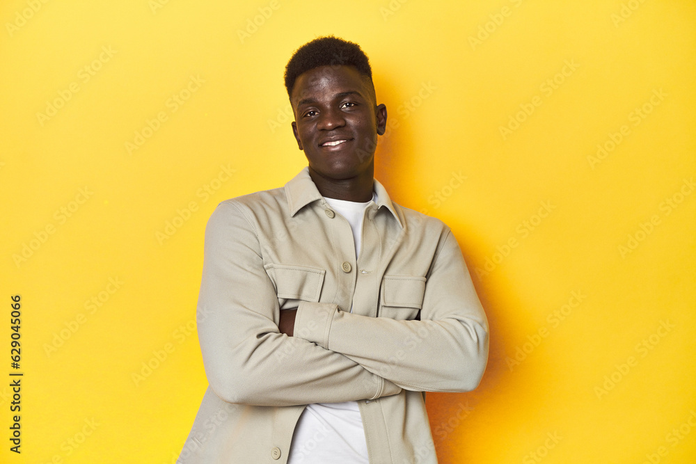 Stylish young African man on vibrant yellow studio background, suspicious, uncertain, examining you.