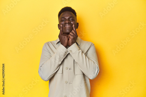 Stylish young African man on vibrant yellow studio background, doubting between two options.