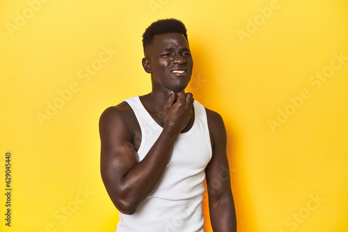 Stylish young African man on vibrant yellow studio background, suffers pain in throat due a virus or infection.