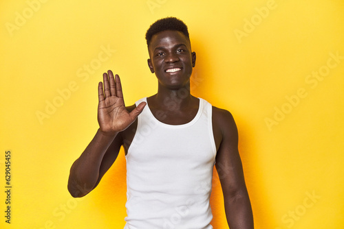 Stylish young African man on vibrant yellow studio background, smiling cheerful showing number five with fingers.