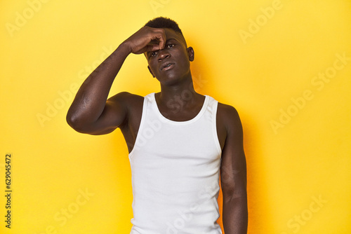 Stylish young African man on vibrant yellow studio background, having a head ache, touching front of the face.