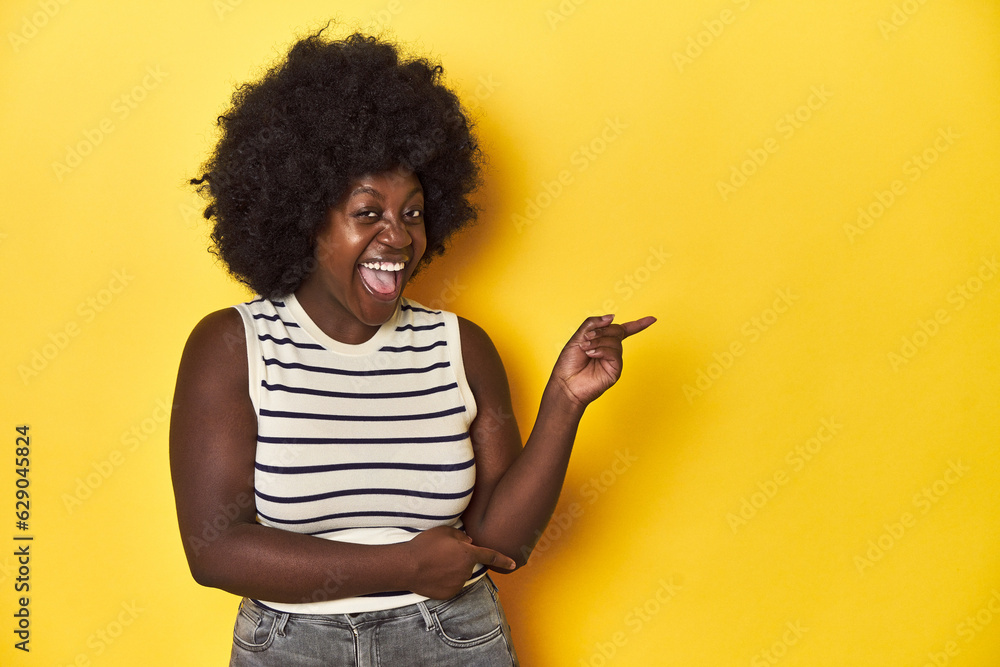 African-American woman with afro, studio yellow background pointing with forefingers to a copy space, expressing excitement and desire. African-American woman with afro, studio yellow background pointing with forefingers to a copy space, expressing excitement and desire.
