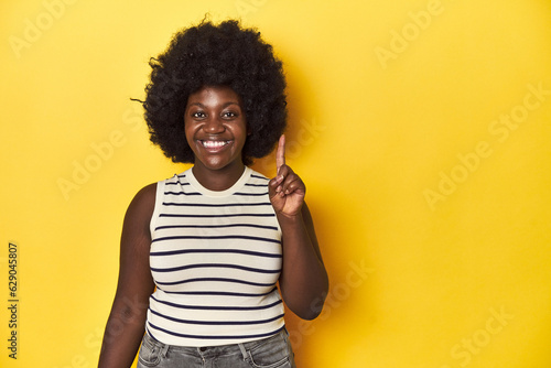 African-American woman with afro, studio yellow background showing number one with finger.