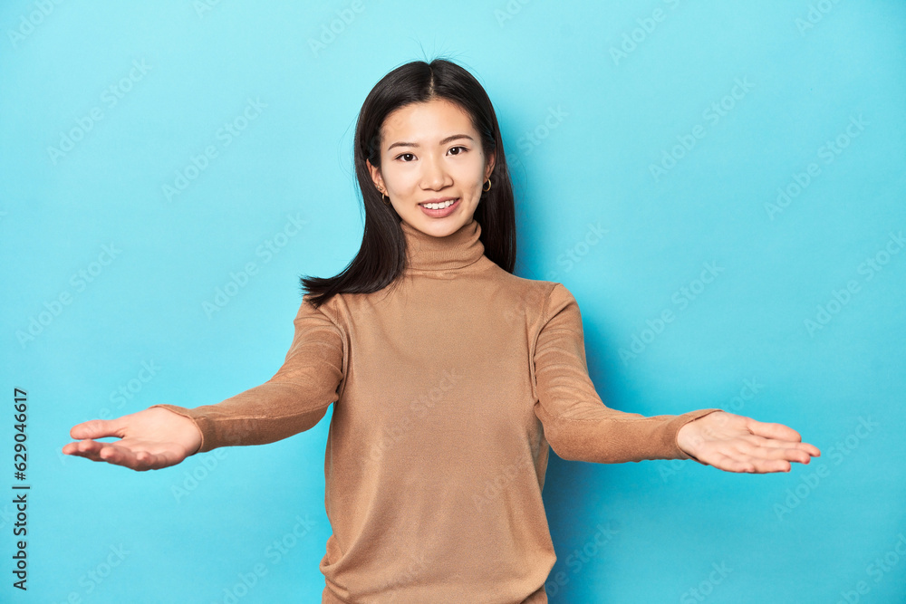 Young Asian woman in brown turtleneck, showing a welcome expression. Young Asian woman in brown turtleneck, showing a welcome expression.