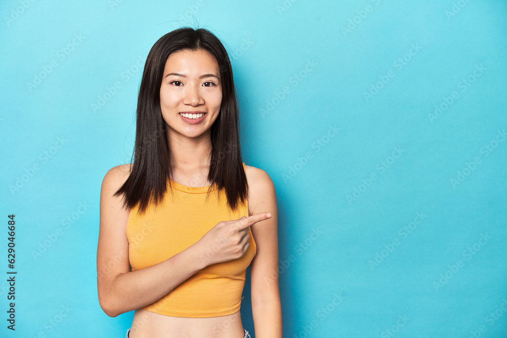 Asian woman in summer yellow top, studio setup, smiling and pointing aside, showing something at blank space. Asian woman in summer yellow top, studio setup, smiling and pointing aside, showing something at blank space.