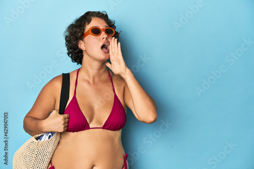 Young woman in bikini with beach bag shouting and holding palm near opened mouth. © Asier