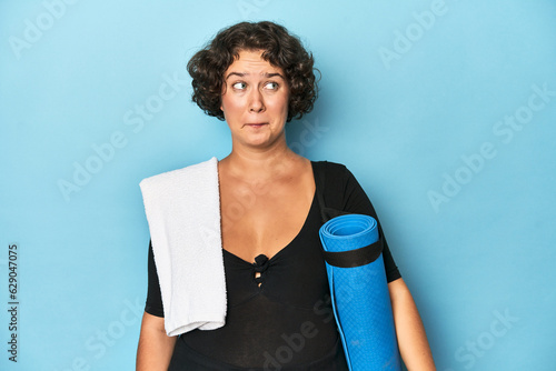 Athletic young woman with yoga mat confused, feels doubtful and unsure.