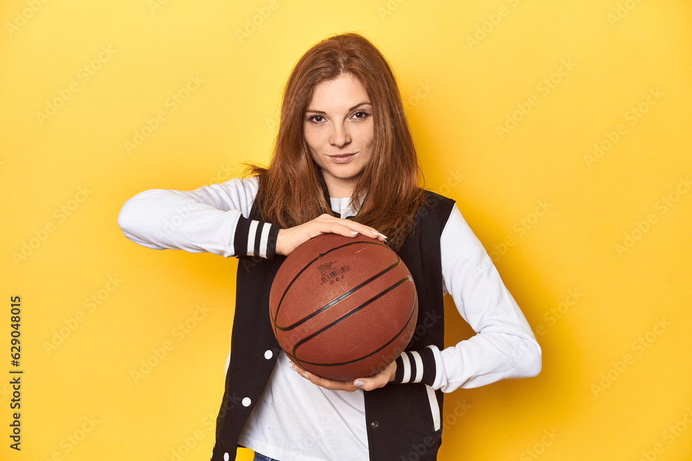 Athletic redhead woman with basketball, yellow studio background. Athletic redhead woman with basketball, yellow studio background.