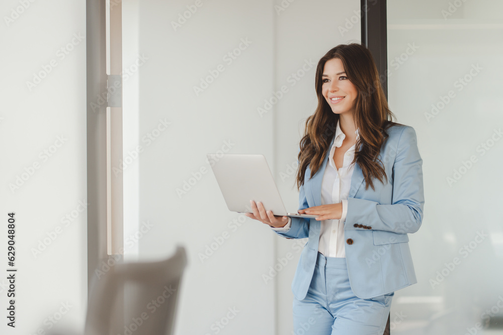 Positive confident smiling businesswoman professional manager using laptop, working online looking at screen in modern office. Freelancer copywriter typing standing at workplace. Technology concept Positive confident smiling businesswoman professional manager using laptop, working online looking at screen in modern office. Freelancer copywriter typing standing at workplace. Technology concept