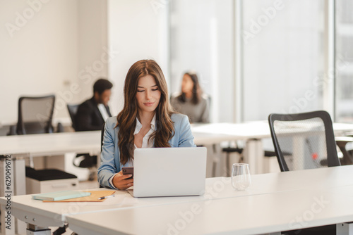 Confident beautiful woman manager using laptop  working online looking at display in modern office. Freelancer copywriter typing  sitting at workplace