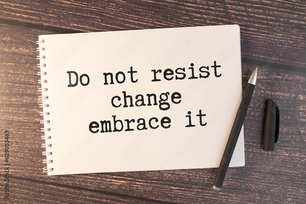 Obraz premium a white notebook with the text Do Not Resist Change Embrace It lies on a wooden surface near.