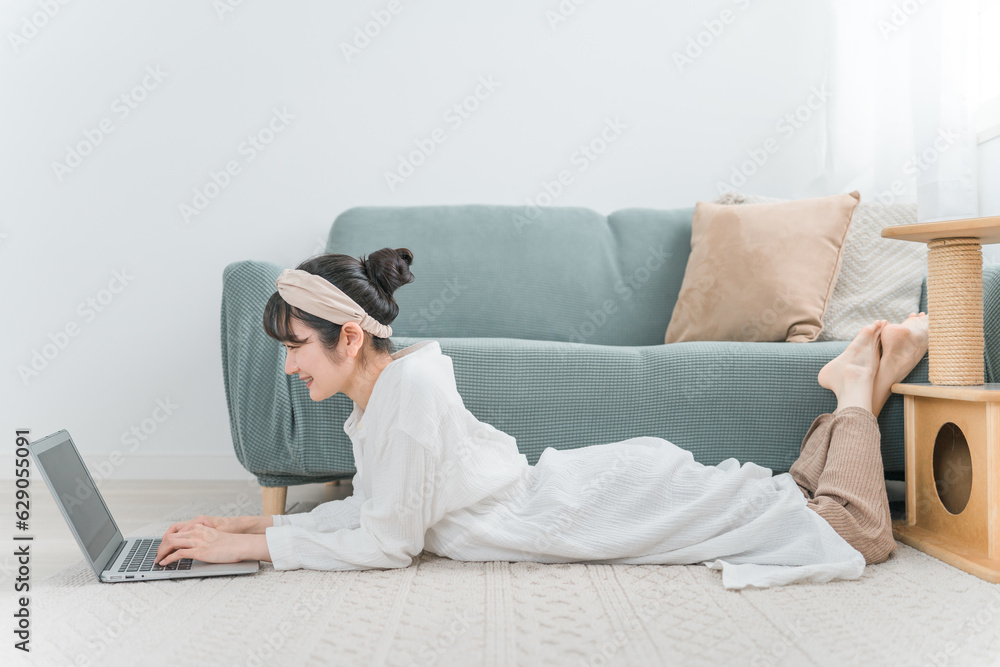 家でくつろぎながらノートパソコンを見るアジア人女性（猫好き・電子書籍・マンガ・動画）

