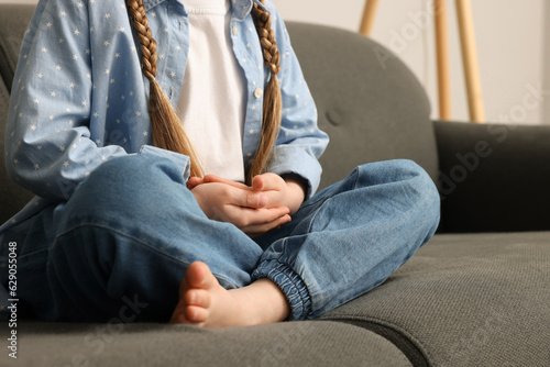 Little girl meditating on soft sofa indoors, closeup