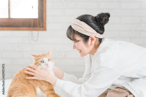 Valokuva ベッドルームで猫・ペットと遊ぶ飼い主のアジア人女性と嫌がる猫