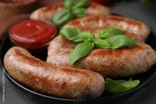 Tasty homemade sausages, ketchup and basil leaves on grey table, closeup