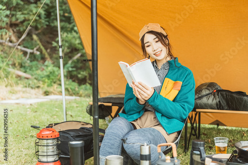キャンプ場でソロキャンプする若い女性キャンパー（読書・本を読む） 