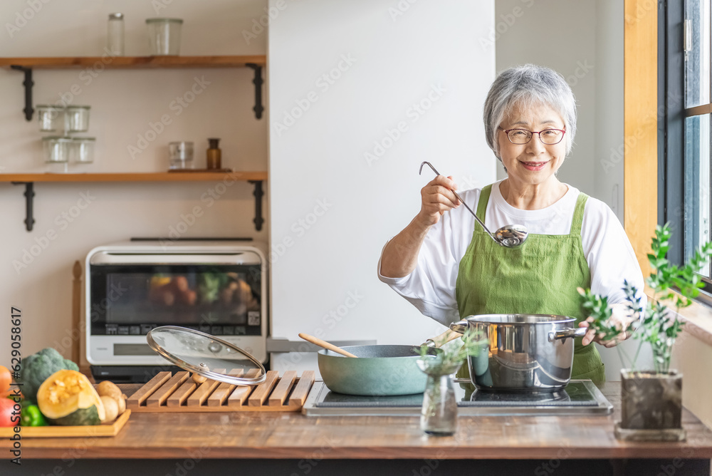 家のキッチンで料理を作るアジア人のシニア・高齢者女性（笑顔）
