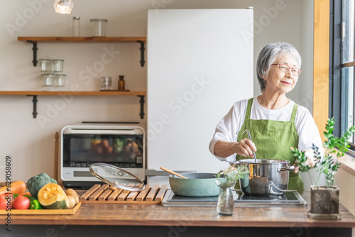 家のキッチンで料理を作るアジア人のシニア・高齢者女性（笑顔）
