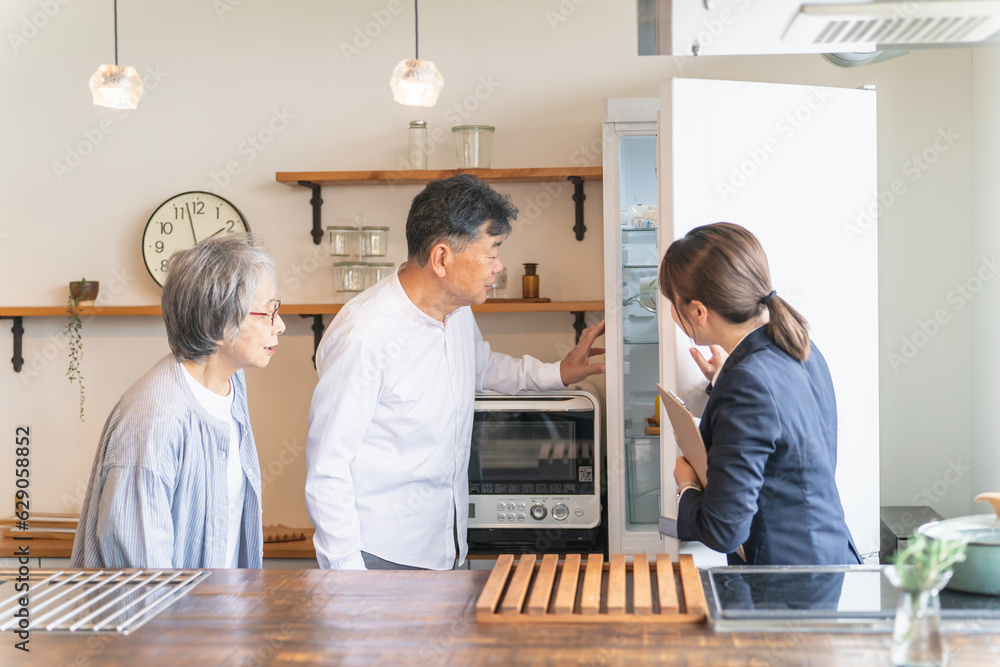 Fototapeta premium 家電量販店・住宅展示場・モデルルーム・電気屋で高齢者夫婦に説明するビジネスウーマン（冷蔵庫） 