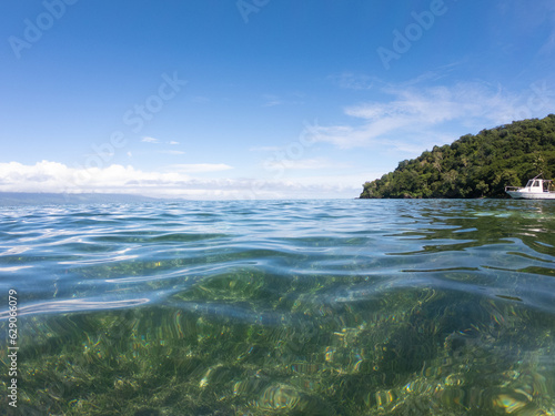 Tranquil calm clear tropical ocean water and blue sky with boat in the background. © Scope Images